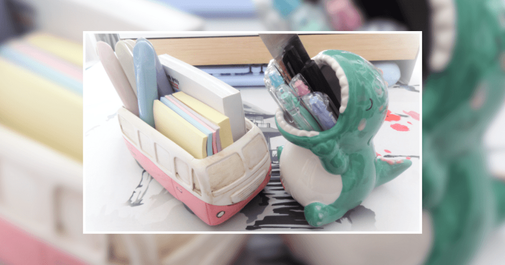 Two desk pots in use; one is shaped like a cute, green dinosaur with its mouth open to hold pens, the other is a pink minibus-shaped pot with its top open for post-it notes.