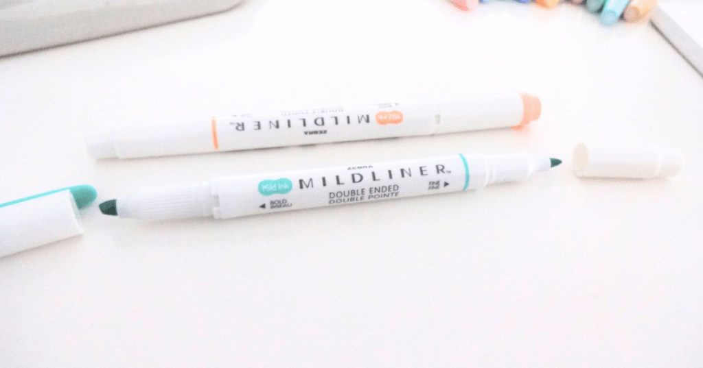 A small variety of Zebra Mildliner highlighters in pastel colors, one of them with both its caps off.