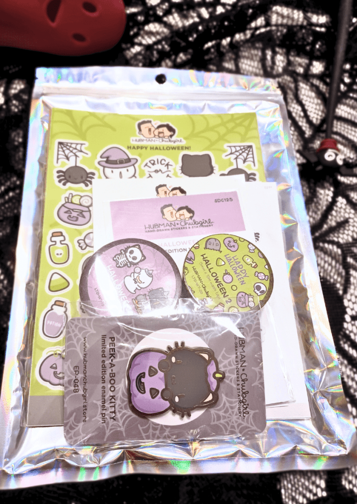 An image showing the packed silver envelope with a transparent top containing the Halloween 2023 bundle from Hubman & Chubgirl.