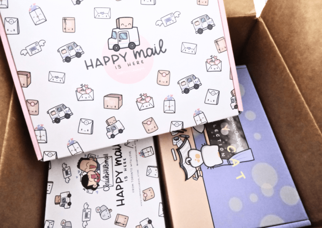 A shipping brown box with three colorful, smaller boxes in it. Two of the boxes are covered in kawaii shipping icons while the third one features a cat sitting on a book and looking outside.