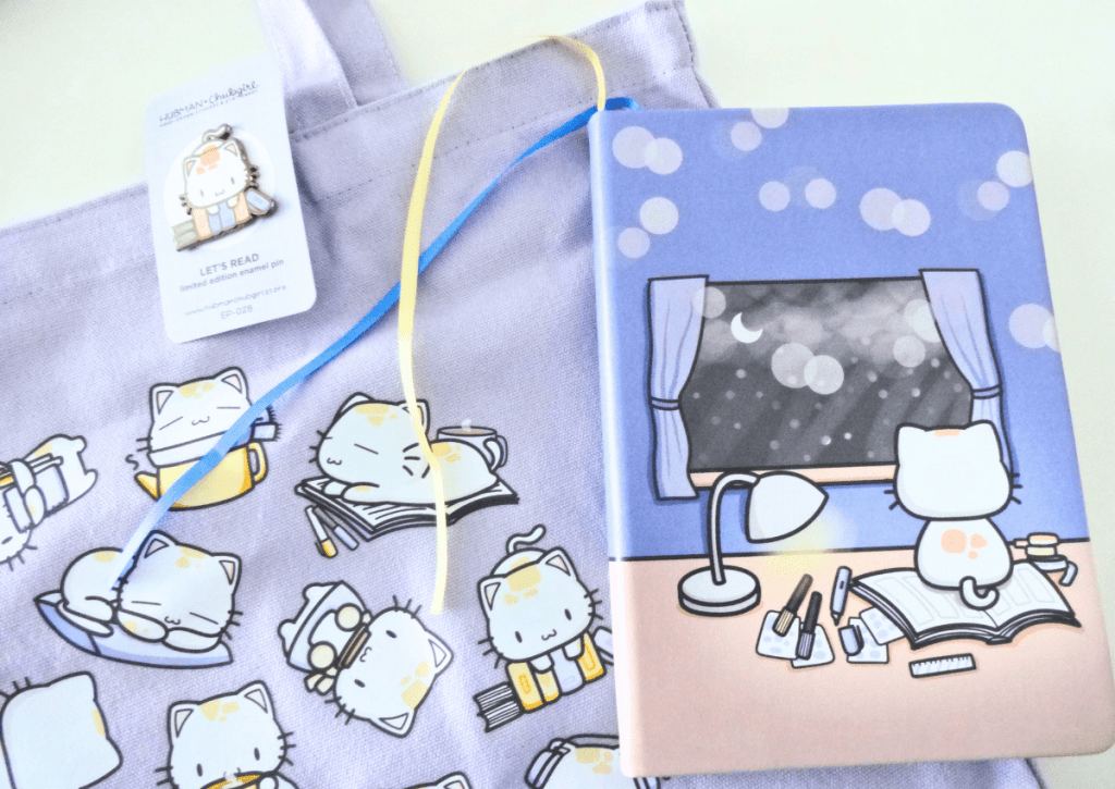 A tote bag, enamel pin, and journal from the Cozy Cat box set.