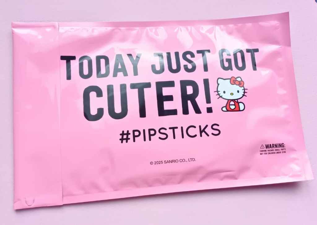 A pink shipping envelope with the words "Today just got cuter!" and "#Pipsticks" along with a depiction of the Hello Kitty character and a Sanrio copyright logo.