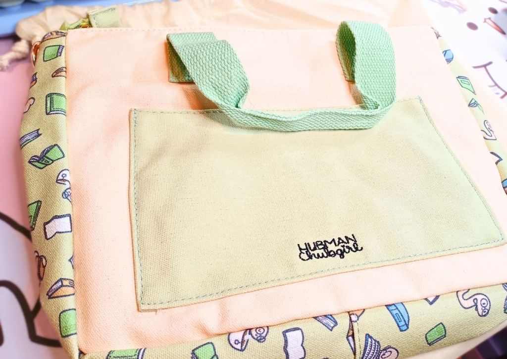 The back of a back with a simple green pocket on a beige background with the words "Hubman & Chubgirl" stitched on it.