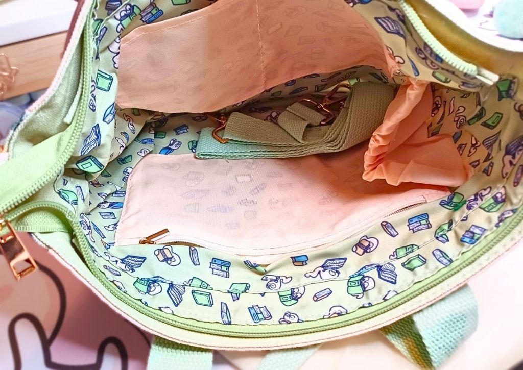 The inside of a bag featuring an array of pockets, and a design of cute worms reading books on a green background.