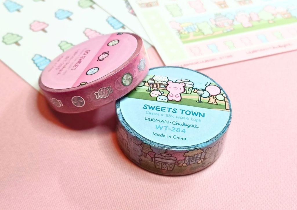 Two rolls of washi tapes still wrapped but showing their designs of cute and colorful candies on the labels stuck to them.