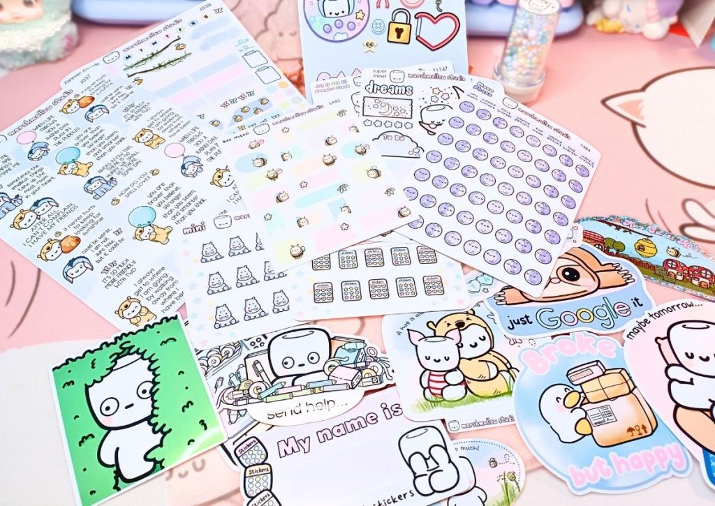 A flatlay of all the cute, colorful, funny and sweet items in this haul: sticker sheets, vinyl stickers, and small stamp.