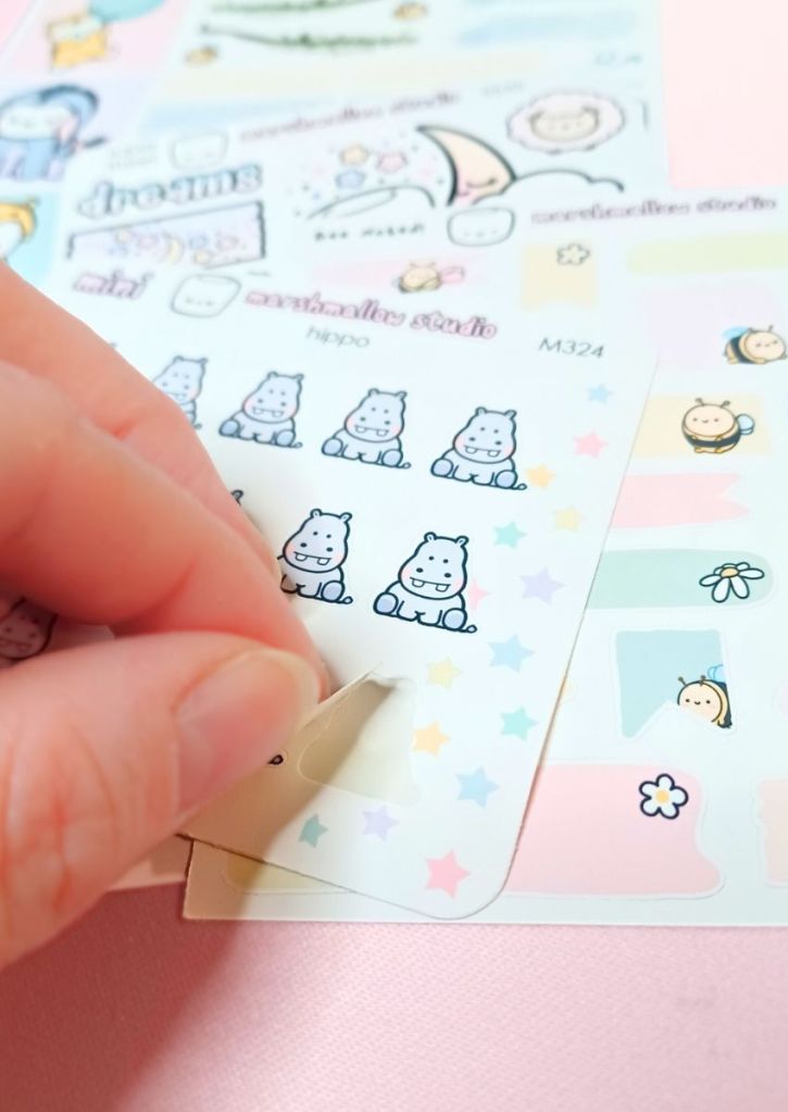 A few cute and colorful sticker sheets with one sticker being peeled, revealing a regular, white backing.
