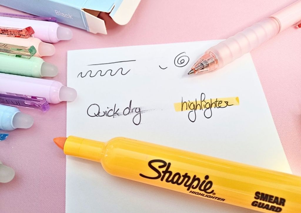 A white sheet surrounded by colorful pens and a yellow highlighter. On the sheet are a few lines, the words "quick dry" and the word "highlighter", the latter being highlighted in yellow.