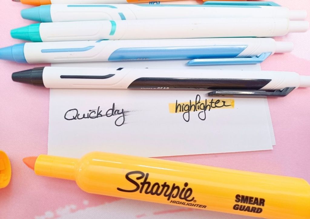 A white sheet surrounded by colorful pens and a yellow highlighter. On the sheet are a few lines, the words "quick dry" and the word "highlighter", the latter being highlighted in yellow.