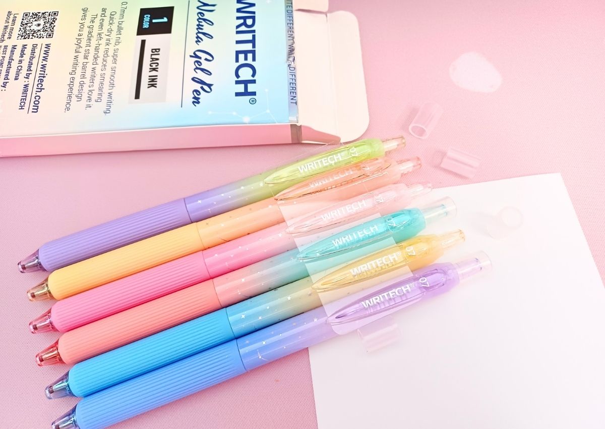 Six colorful pens with a stars and constellations on them are placed next to their box, still clinging to a small plastic sheet to keep their formation intact.