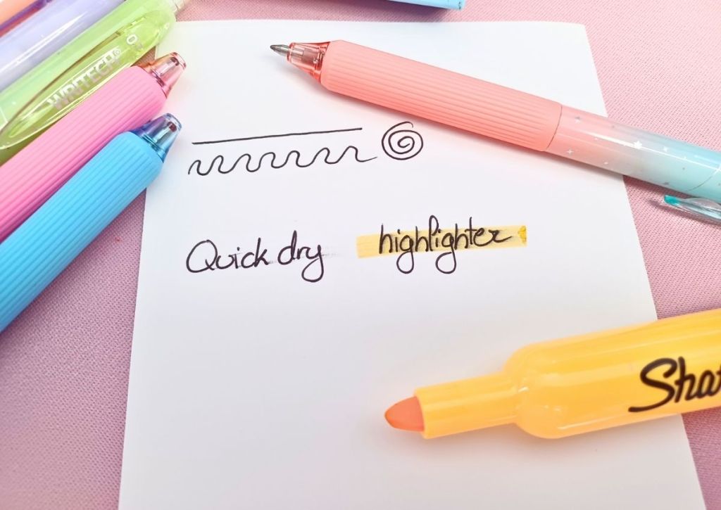 A white sheet surrounded by colorful pens and a yellow highlighter. On the sheet are a few lines, the words "quick dry" and the word "highlighter", the latter being highlighted in yellow.