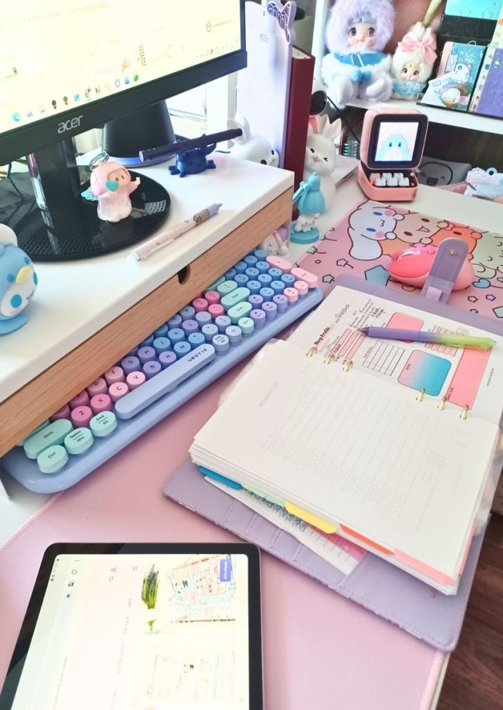 A pastel color desk and items, and a small binder opened to a colorful page with a pen placed upon it.