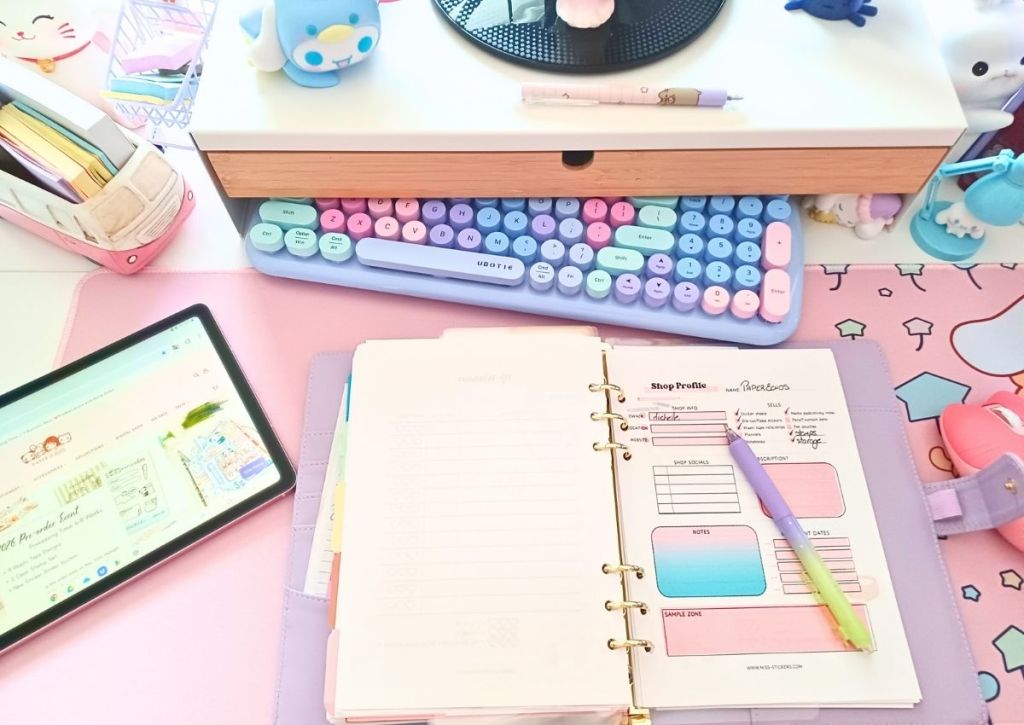 Flatlay of a pastel color desk and items, and a small binder opened to a page called Shop Profile with a pen placed upon it.