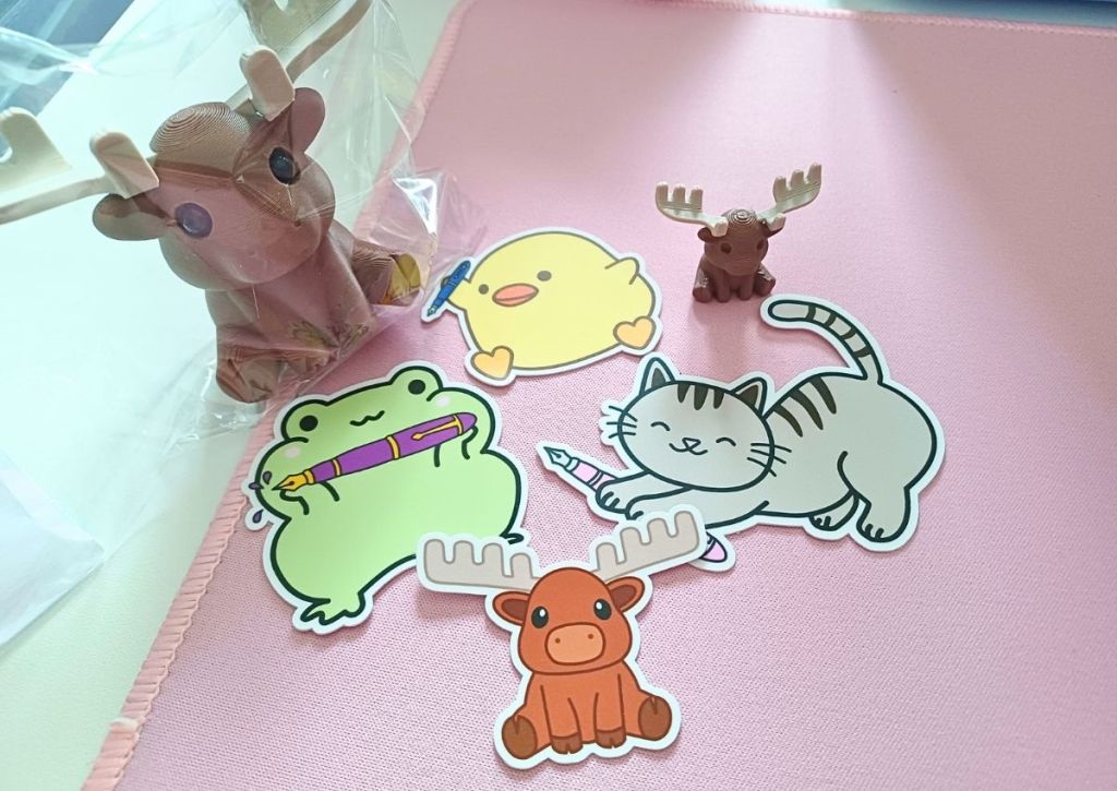 A moose pen-holder, a mini-moose, and colorful vinyl stickers of animals holding fountain pens.