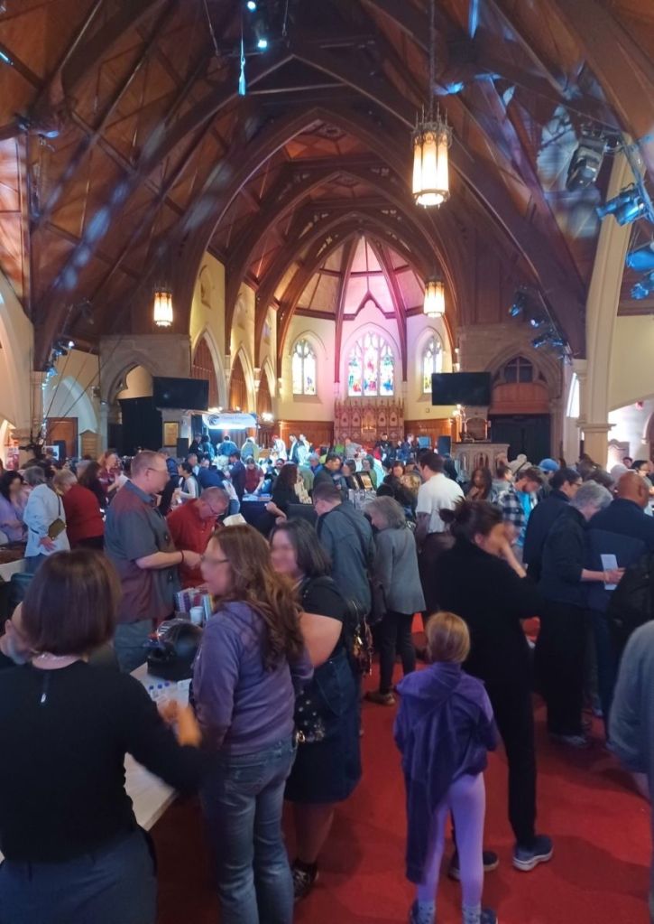 A church's brown interior and lots of people crowding show tables displaying fountain pens.