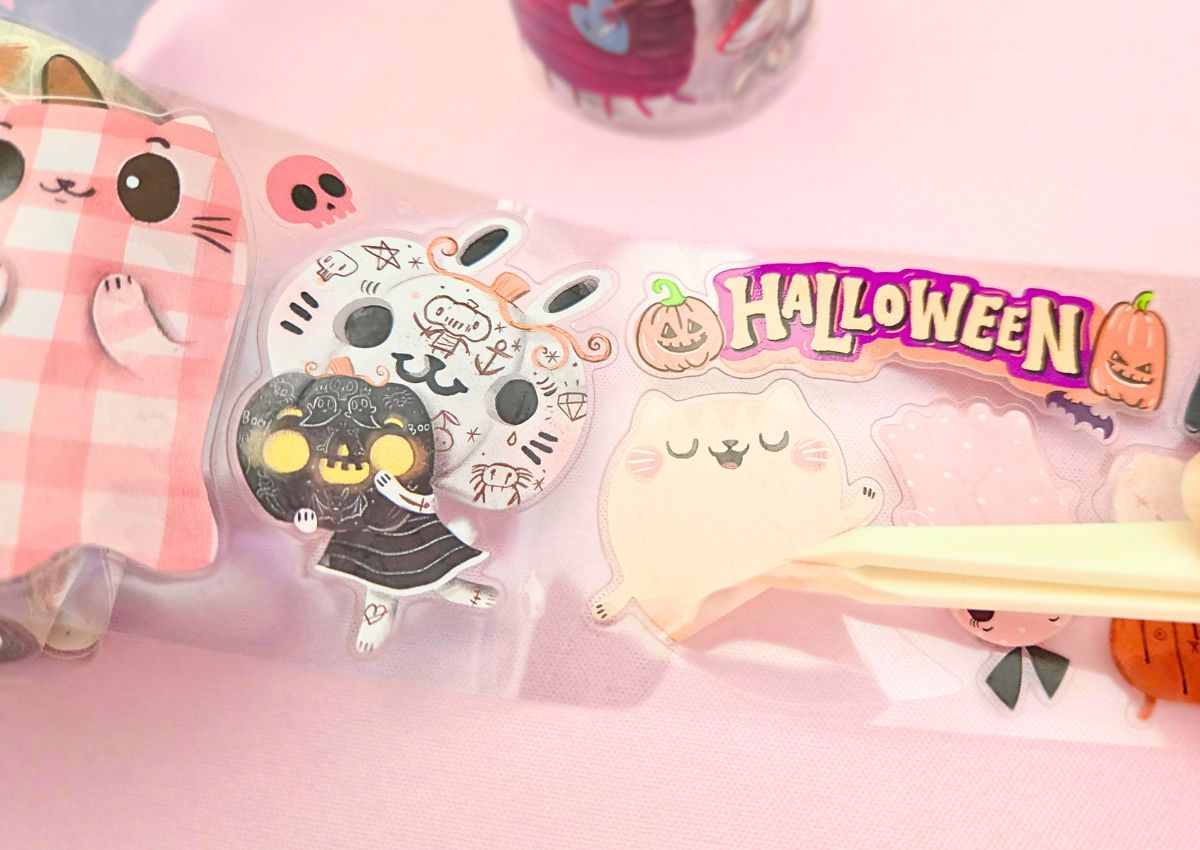 A cute cat ghost sticker being peeled off a PET tape background.