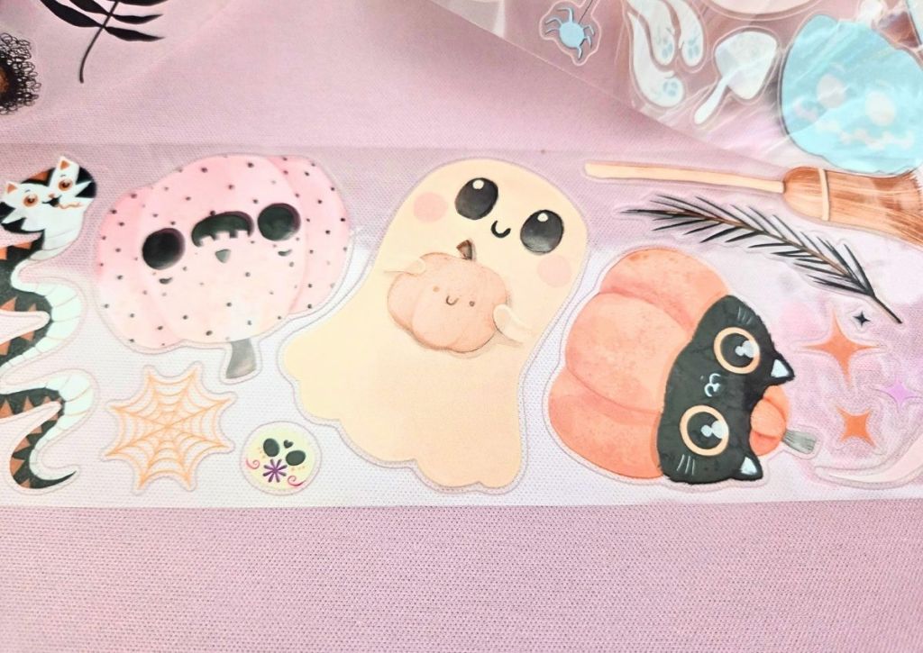 Cute pastel Halloween stickers on PET tape rolls featuring a pink polka dot pumpkin, a smiling ghost holding a pumpkin, and a black cat with big eyes hiding inside a pumpkin.