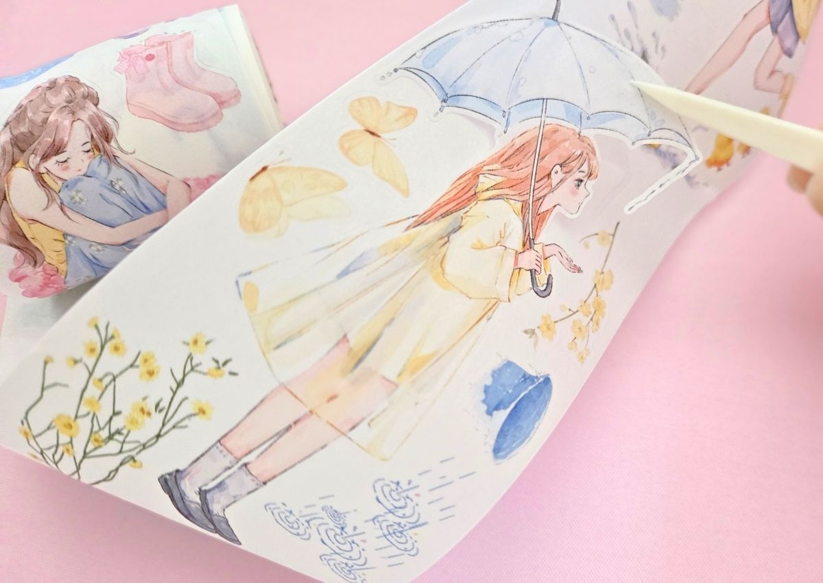 The sticker of a girl wearing a yellow transparent raincoat and holding an umbrella being peeled off a washi tape roll.