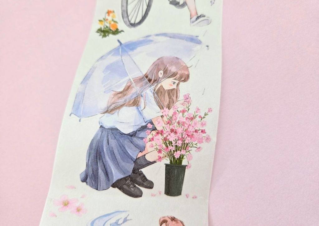 A girl crouching next to pink flowers in a vase and holding a big umbrella.