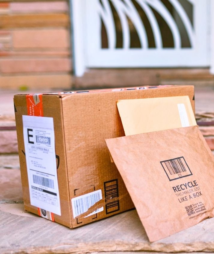 A cardboard box and two envelopes are placed on a stone porch in front of a house door. 