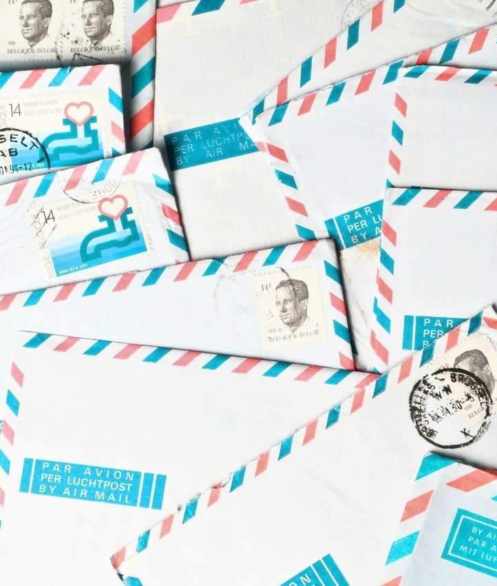 A pile of vintage airmail envelopes with red and blue borders, postage stamps, and postmarks scattered in an overlapping arrangement.
