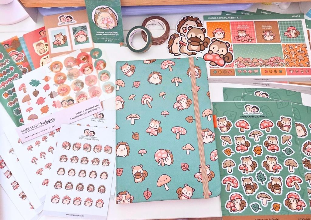 Assorted stationery items with cute hedgehog, mushroom, and woodland themes, including stickers, a teal notebook, planner kits, washi tape, and decorative sheets arranged on a flat surface.