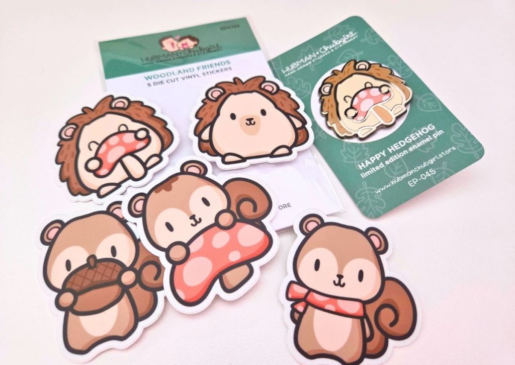 Five cute vinyl stickers and one pin featuring cartoon hedgehogs and squirrels with mushrooms and scarves, displayed on a white surface alongside product packaging.
