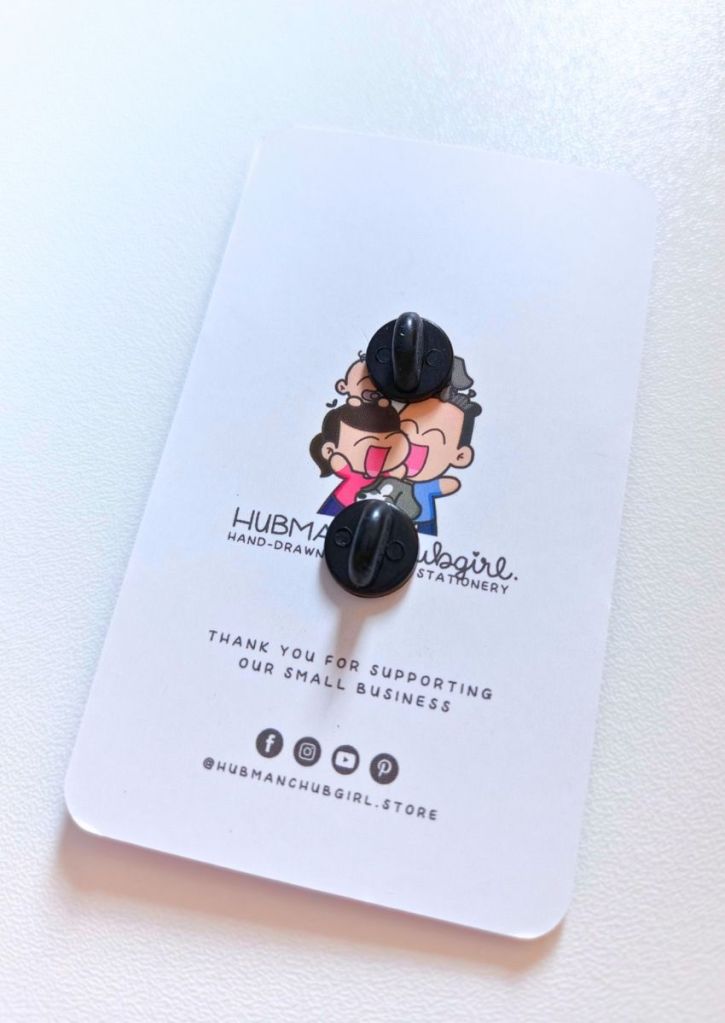 A pin backing card with cartoon art of a smiling character, two black pin backs, and text thanking customers for supporting the small business, Hubman & Chubgirl. Social media icons are shown at the bottom.