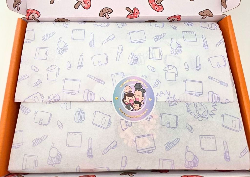 A box lined with mushroom-patterned paper, containing tissue paper decorated with digital art icons and sealed with a round sticker featuring cartoon characters.