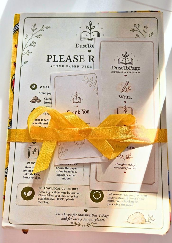 A DustToPage stone paper journal package tied with a yellow ribbon, featuring a thank-you note and instructional cards with illustrations of books and plants.