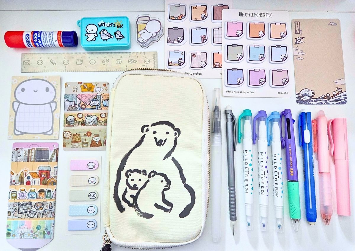 A collection of stationery supplies including sticky notes, a ruler, a glue stick, mildliner markers, pens, and a canvas pencil case featuring an illustration of a mother polar bear with two cubs.