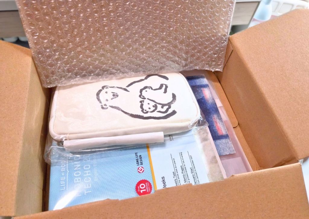 Cardboard box containing a planner and a canvas pencil case with a drawing of a bear and cubs.
