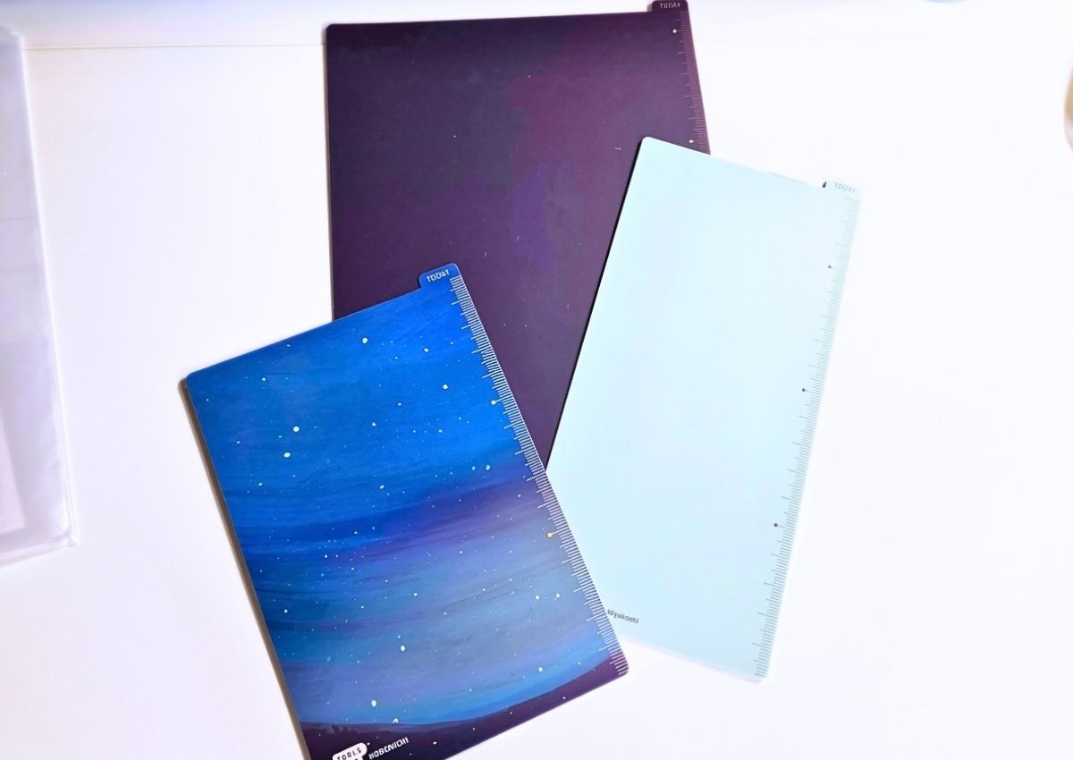 Three Hobonichi planner page marker boards featuring a starry night design, a solid dark purple, and a solid pale blue.