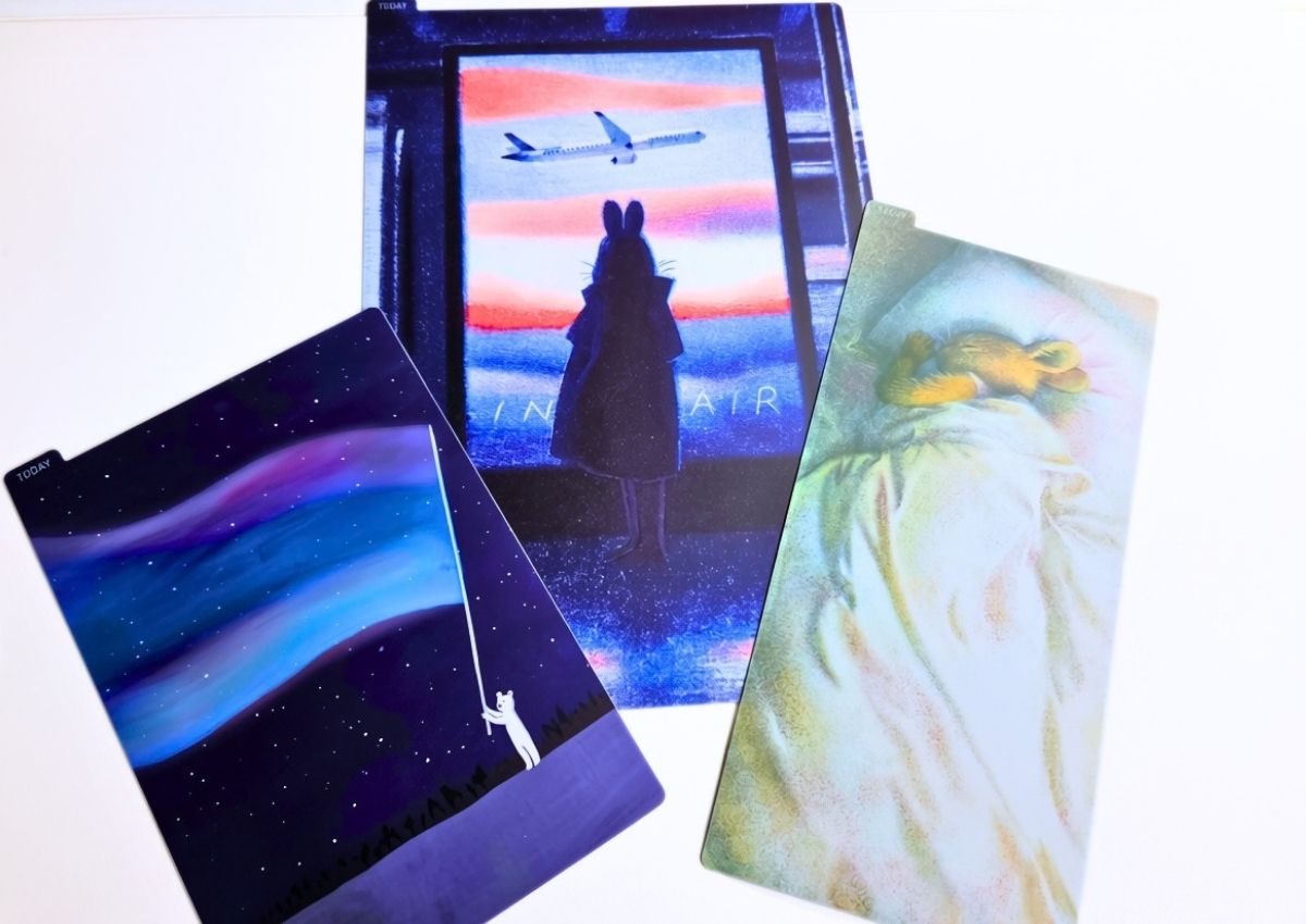 Three rectangular index tabs featuring illustrations: a bear under the aurora borealis, a rabbit watching a plane at sunset, and a small bunny sleeping under a blanket.