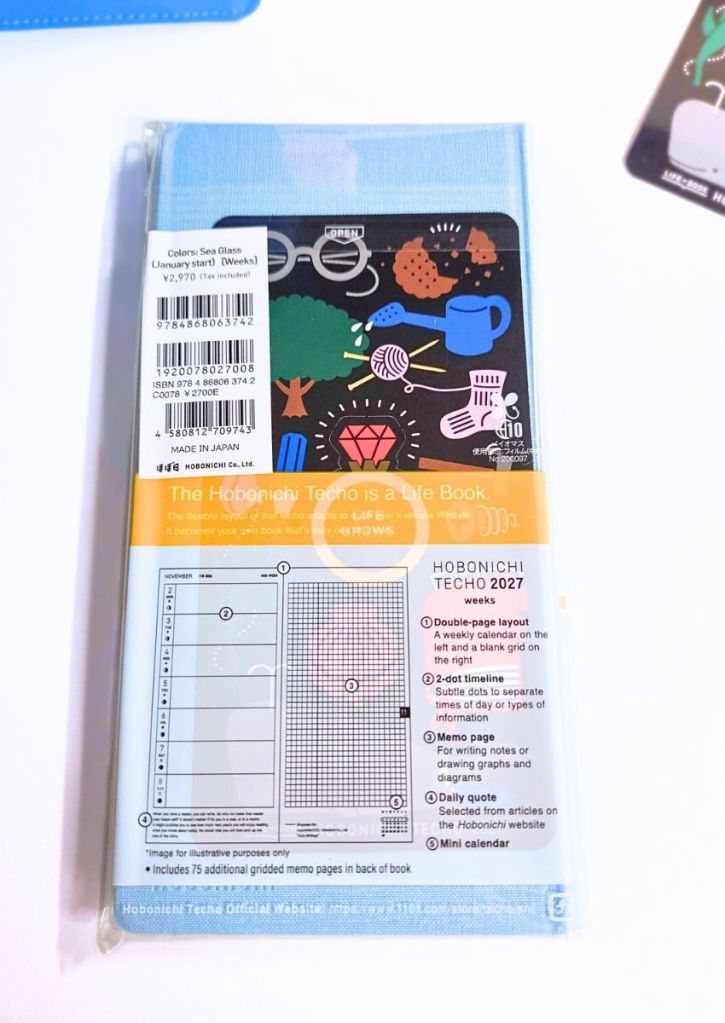 A Hobonichi Techo 2027 weeks planner in its plastic packaging, showing the back cover with product details and a diagram of the weekly grid layout.