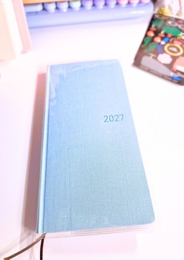 A light blue 2027 planner on a white desk.