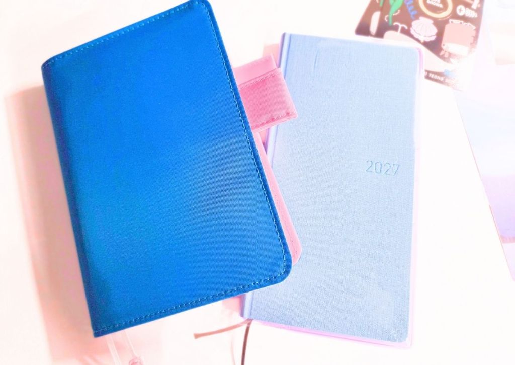 A bright blue planner cover and a light blue planner labeled 2027 sitting on a white surface.